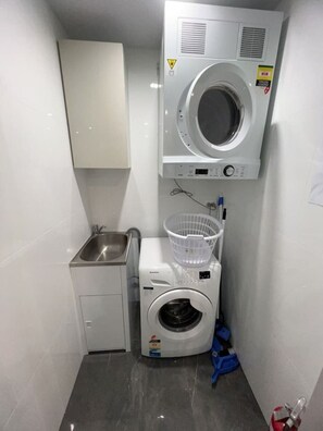 A compact laundry room with a washing machine, a dryer, a sink, and a small cabinet. - Meriton L47 with SeaViews and CarPark (Surfers Paradise)