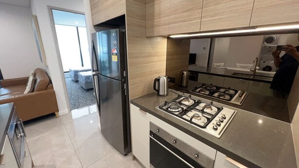 A modern kitchen with a stainless steel refrigerator, gas stove, and a coffee maker. - Meriton L47 with SeaViews and CarPark (Surfers Paradise)