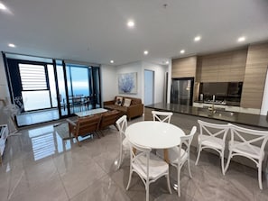 A modern kitchen with a central island, dining area with white chairs, and a large window providing a view. - Meriton L47 with SeaViews and CarPark (Surfers Paradise)