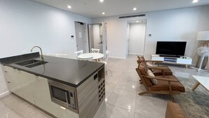 A modern kitchen with a central island, a dining area with chairs, a sofa, a flat-screen TV, and a fan. - Meriton L47 with SeaViews and CarPark (Surfers Paradise)