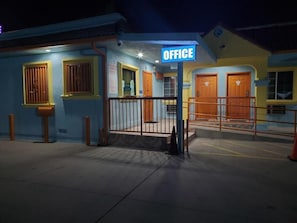 Un edificio con un cartel que dice 'OFFICE' en la entrada, un acceso con portones y una escalera que conduce al edificio principal.