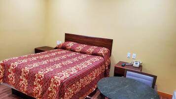 A hotel room with a bed, bedside tables, a round table, and a chair.