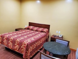 Una habitación de hotel con cama, mesitas de noche, una mesa redonda y una silla.