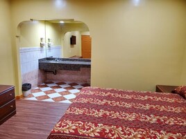 Habitación de hotel con piso a cuadros, una cama con cubrecama estampado, un mesita de noche de madera y un baño con pared de azulejos y un lavamanos.