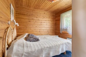 A wooden cabin bedroom with a bed, pillows, a headboard, and a window with curtains.
