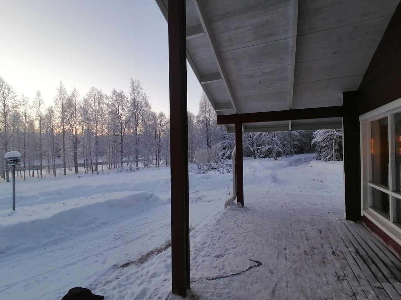 A covered outdoor area with a view of a snowy landscape and trees.