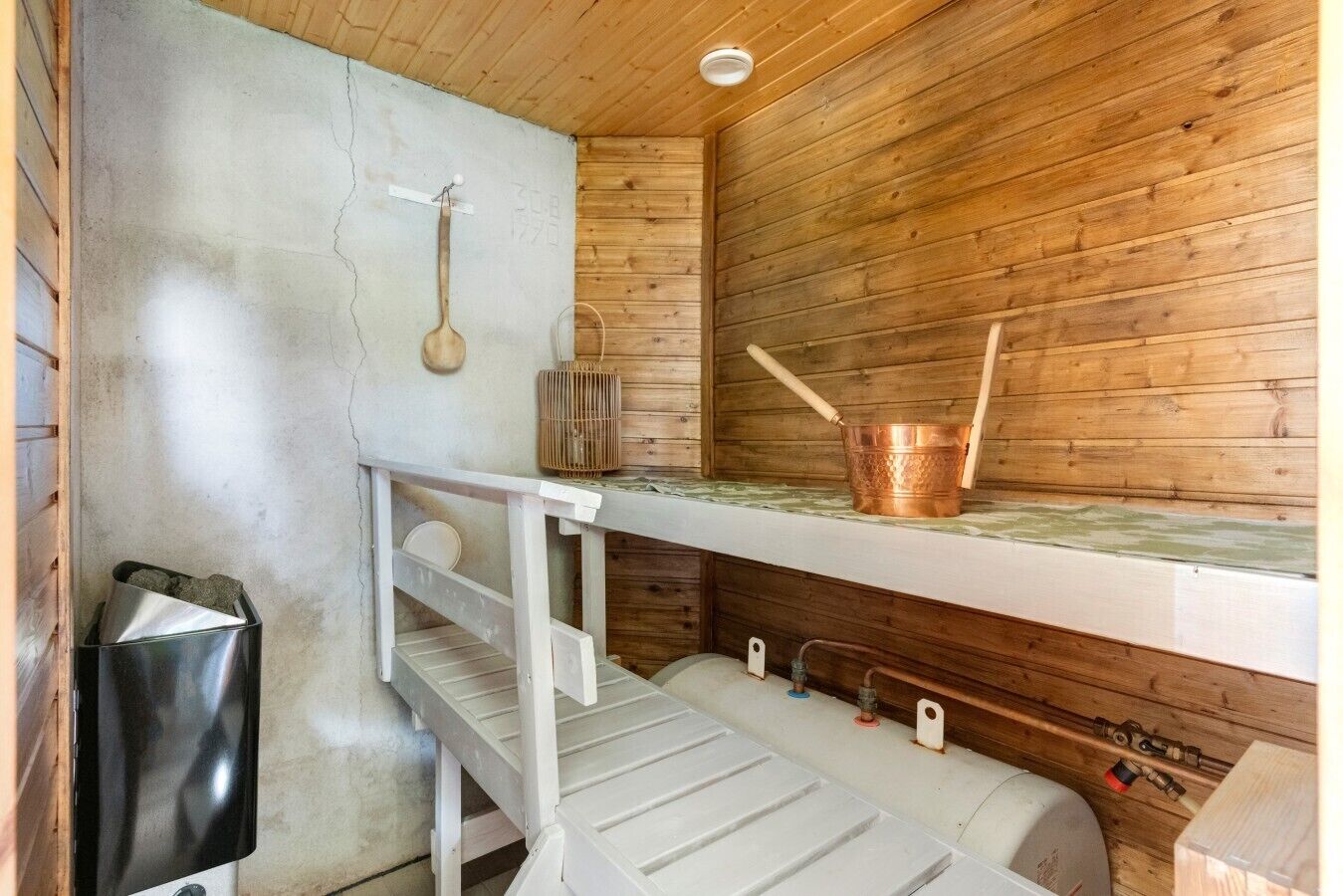 Un sauna con paredes de madera, un banco, una cuchara de madera y un balde de cobre.