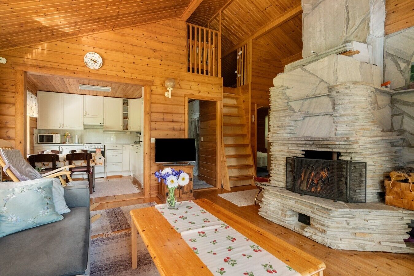 A cozy cabin interior with a stone fireplace, wooden furniture, and a kitchen area.