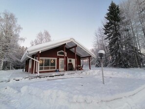 A wooden cabin with a covered porch and a snow-covered landscape.