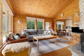 A wooden cabin interior with a sofa, armchairs, a dining table, and a kitchen area.