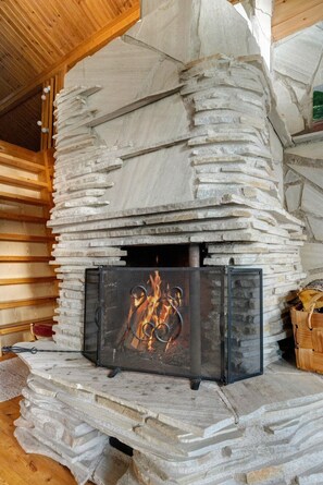 A stone fireplace with a metal screen, surrounded by wooden logs.