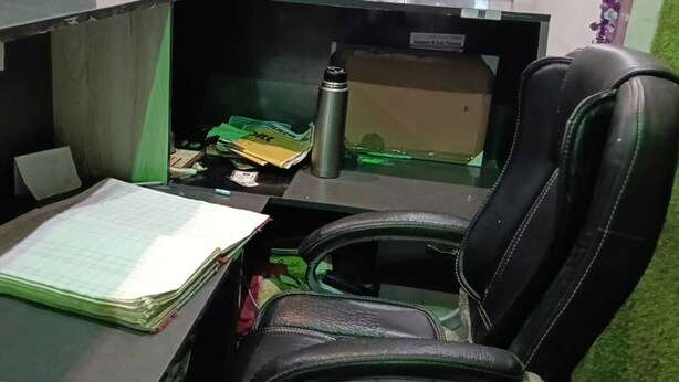 A desk with a chair, a stack of papers, a thermos, and some boxes. - The Singh Hotel (Auraiya)