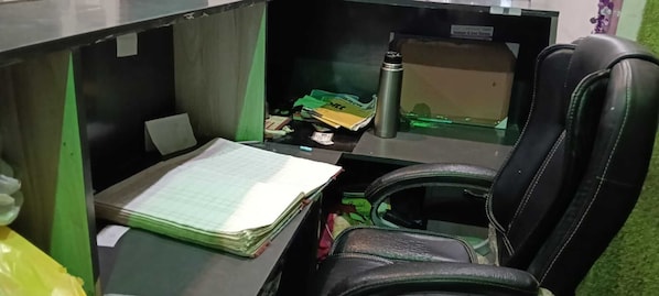 Un escritorio con una silla, una pila de papeles, un termo y algunas cajas.
