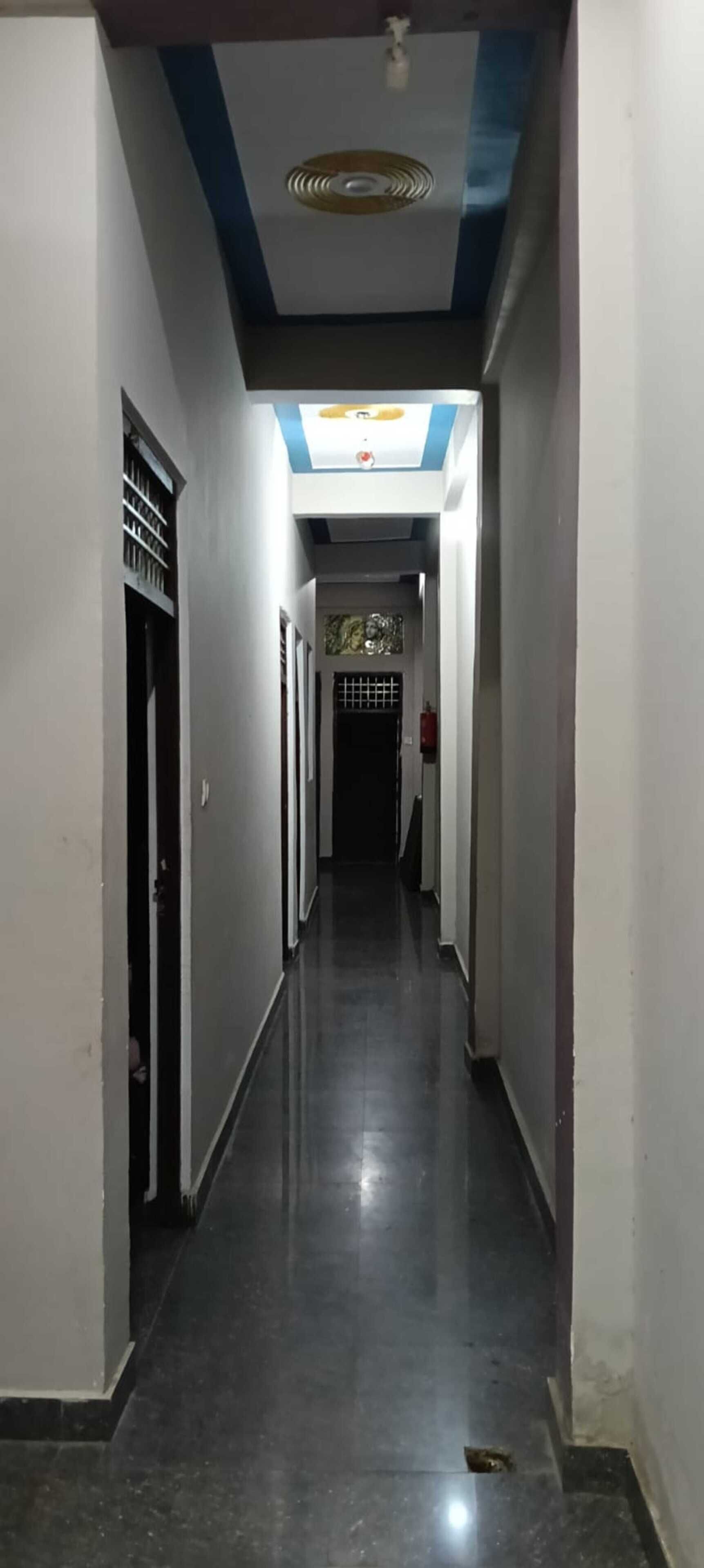 Un long couloir étroit, avec des portes de chaque côté, un ventilateur de plafond et un extincteur fixé au mur.