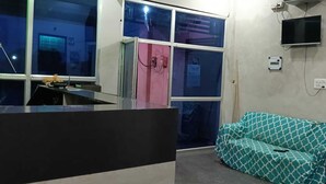 A room with a kitchenette, a sofa, a TV mounted on the wall, and a window with curtains. - The Singh Hotel (Auraiya)