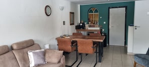 Ein Wohnzimmer mit Sofa, einem Esstisch mit Stühlen, einer Küchenzeile mit Geräten und einer Tür.