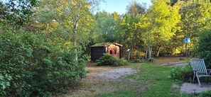 Eine kleine Holzhütte, umgeben von dichtem Grün, einem Vogelhaus und einer Bank.