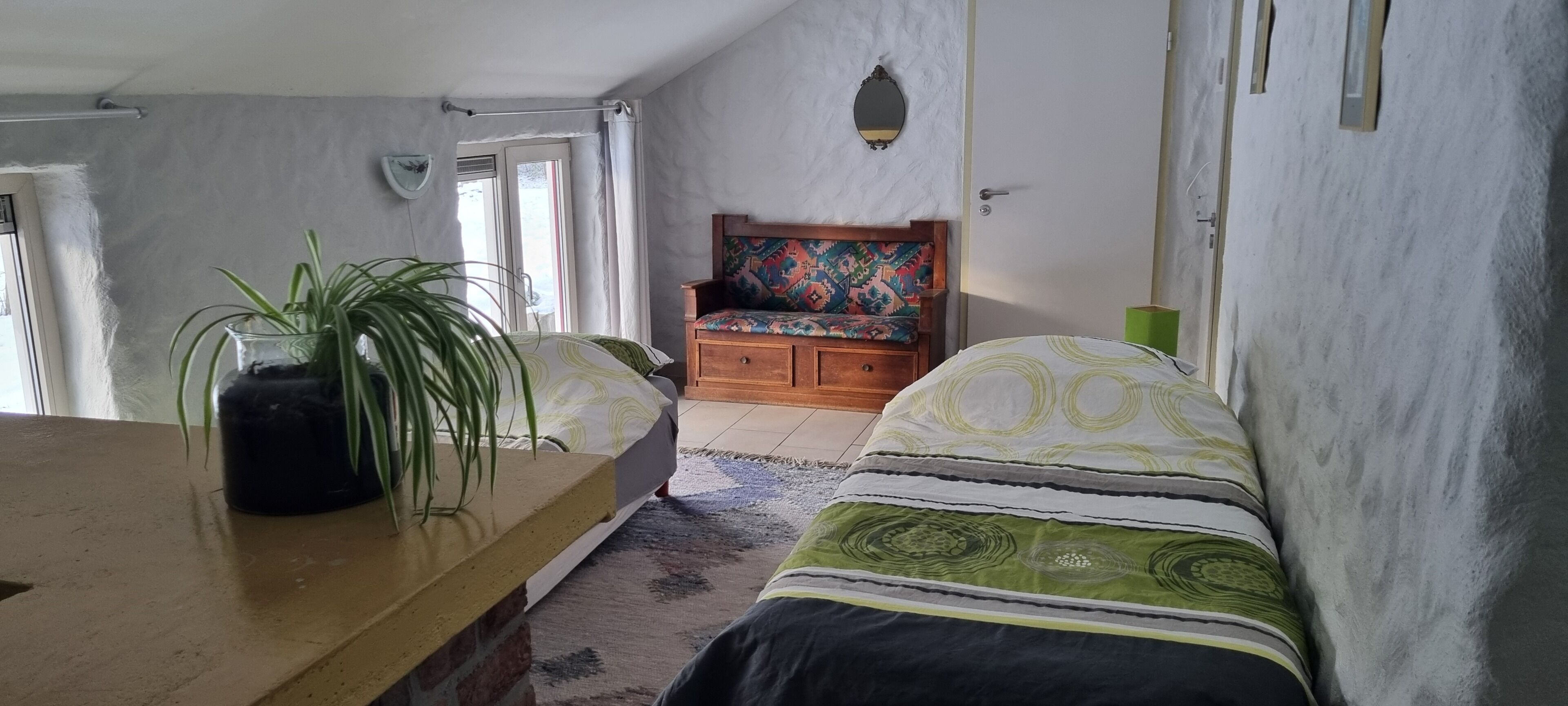Une pièce comprenant un lit, un banc en bois, une plante en pot, un miroir et une porte.