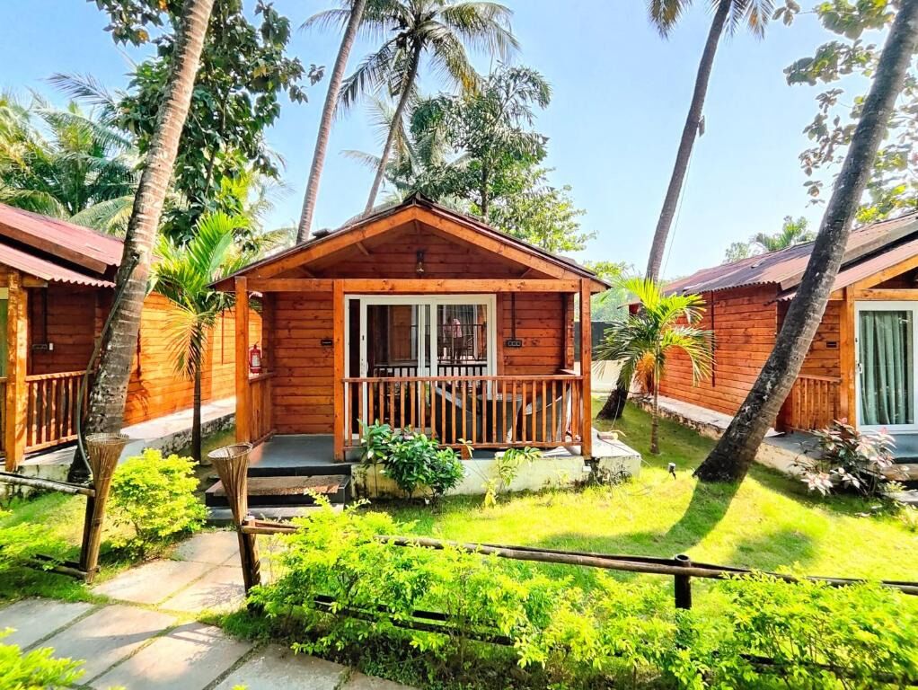 A wooden cabin with a porch, surrounded by palm trees and greenery.