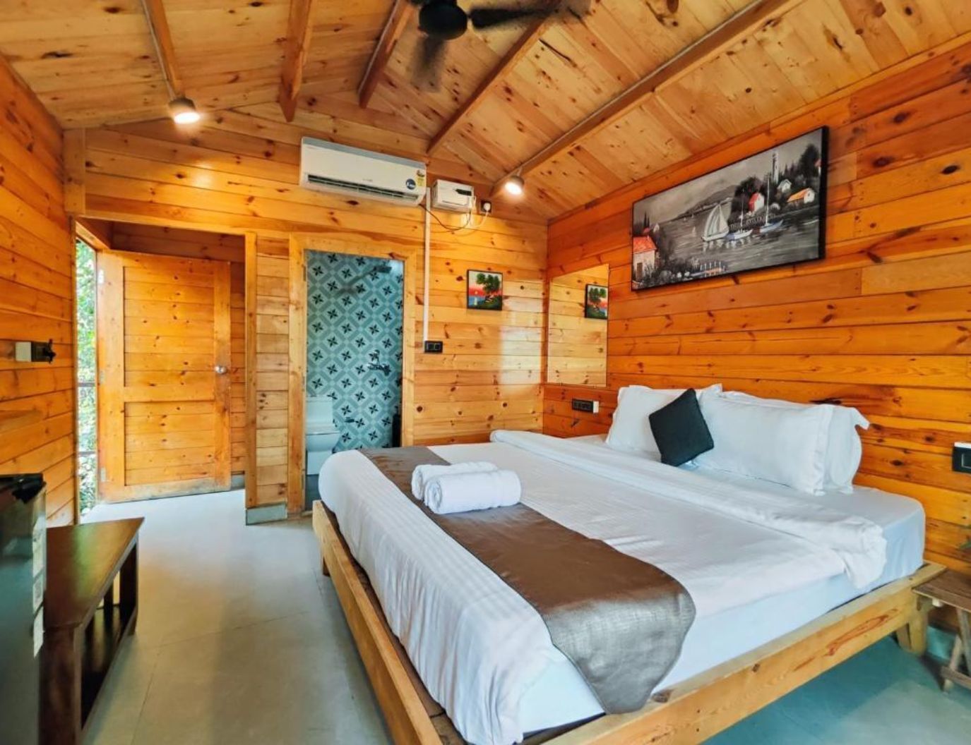 Ein Zimmer in einer Holzhütte mit einem Bett, einer Klimaanlage und einem Gemälde an der Wand.