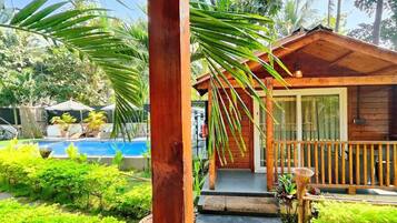 A wooden cabin with a porch, a swimming pool, and lush greenery.
