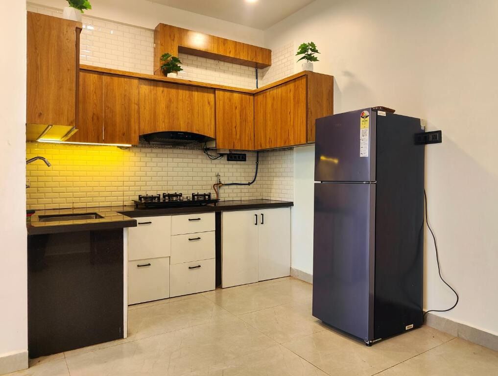 Eine Küche mit Holzschränken, einem schwarzen Kühlschrank und einer gefliesten Spritzschutzwand.