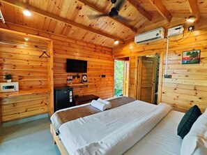 A wooden cabin room with a bed, a desk, a television, and an air conditioning unit. - Trideus Riviera - Riverside Resort, Candolim Goa (Candolim)