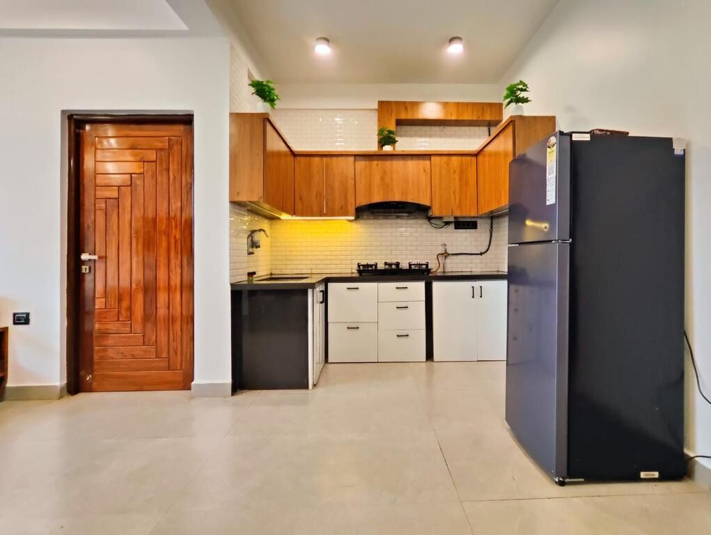 Una cocina con armarios de madera, un refrigerador negro y piso de baldosas.