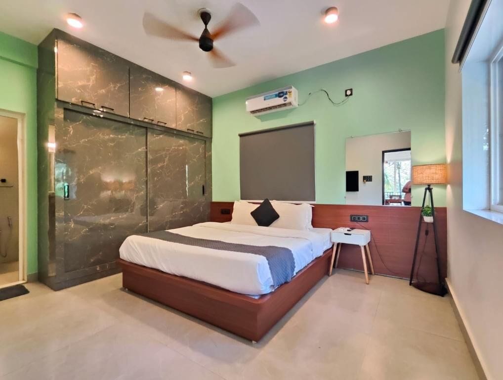 Una habitación de hotel moderna con una cama grande, ventilador de techo, unidad de aire acondicionado, mesita de noche y ventana con vistas.