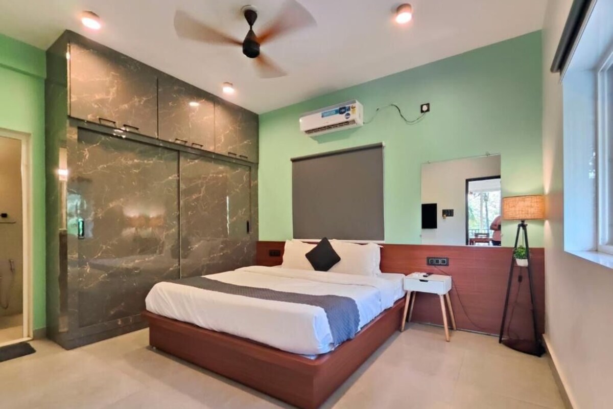 Una habitación de hotel moderna con una cama grande, ventilador de techo, unidad de aire acondicionado, mesita de noche y ventana con vistas.