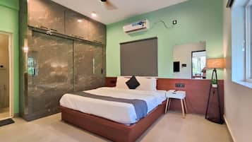 Una habitación de hotel moderna con una cama grande, ventilador de techo, unidad de aire acondicionado, mesita de noche y ventana con vistas.