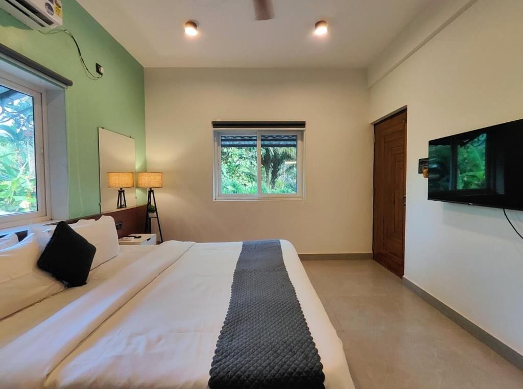 A hotel room with a bed, a window, a television, and a door.