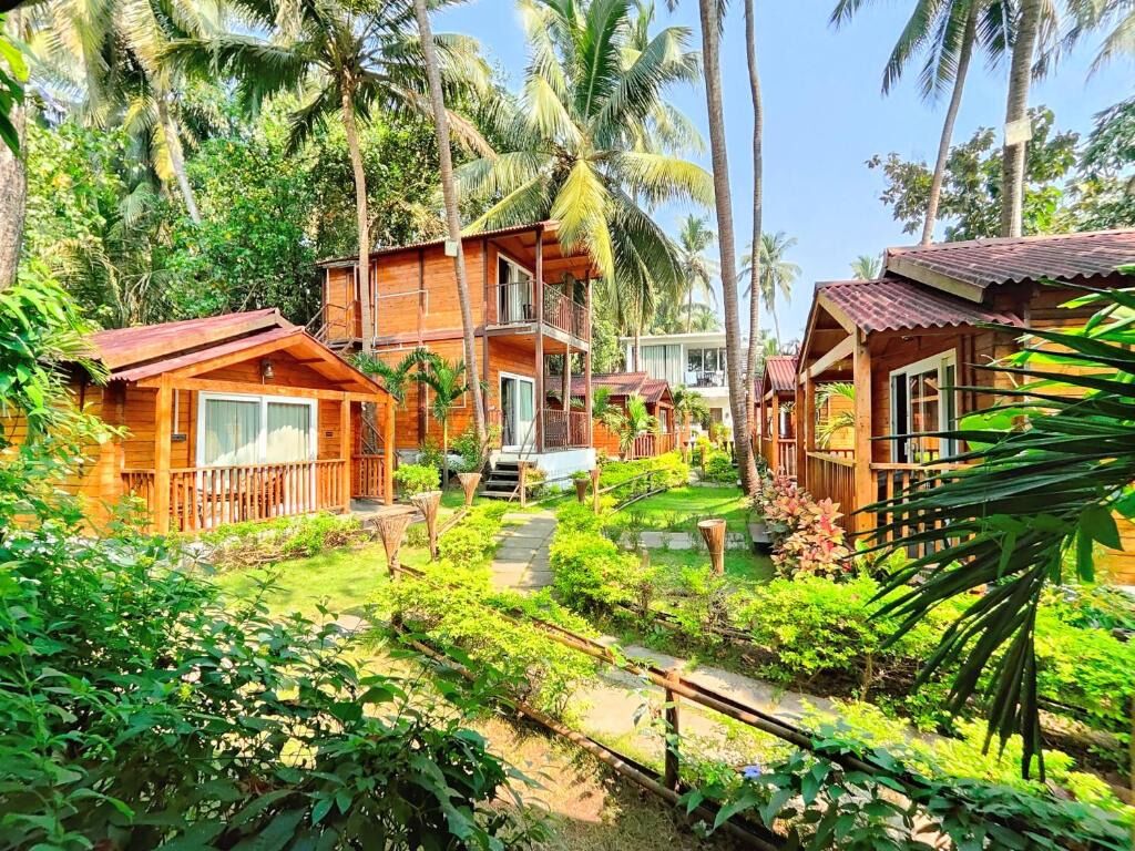 Un bungalow in legno con balcone, immerso nel verde e circondato da palme.
