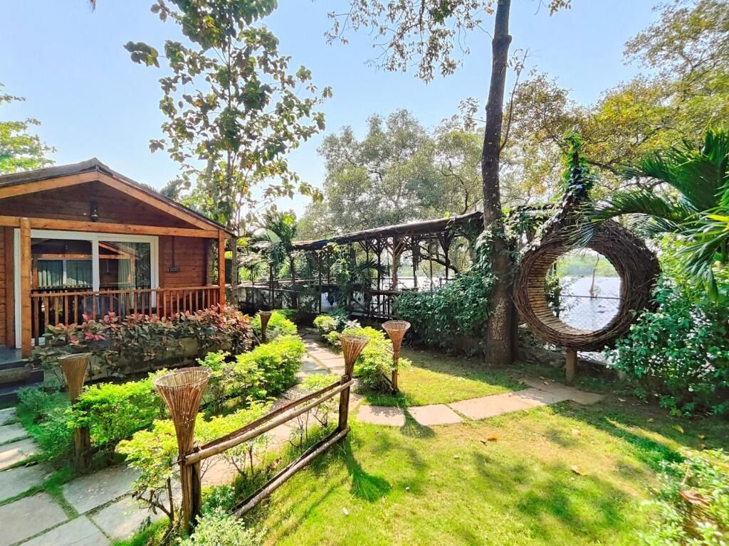 Uma cabana de madeira com varanda coberta, rodeada por vegetação exuberante e uma estrutura circular de fibra natural.