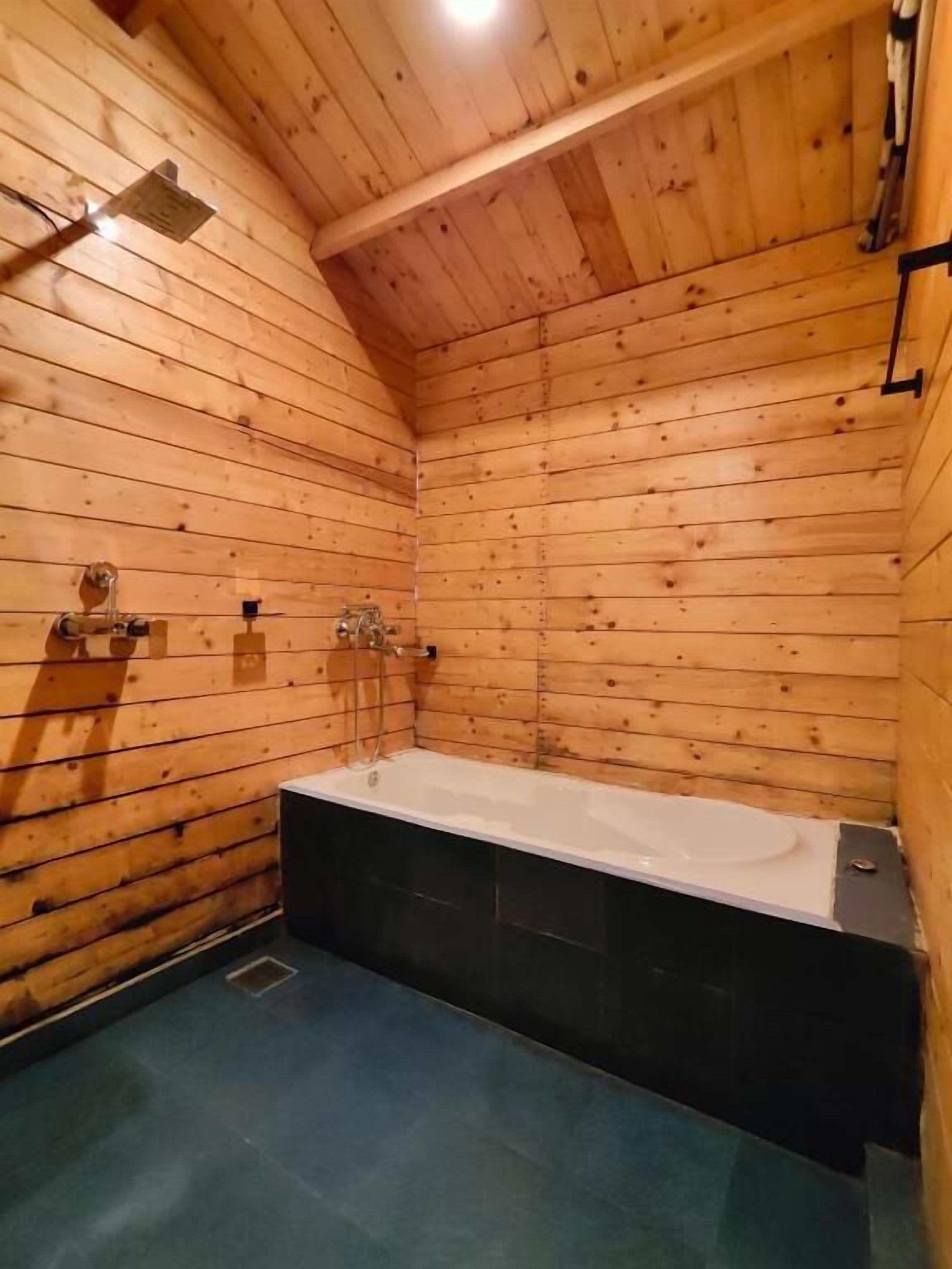 Une salle de bain rustique, située dans une cabane en bois, avec une baignoire, des murs en bois et un plafond en pente.