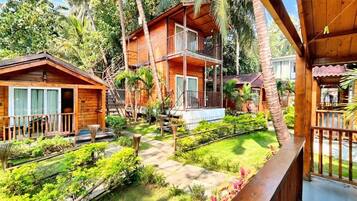A wooden cabin with a balcony, surrounded by lush greenery and palm trees.