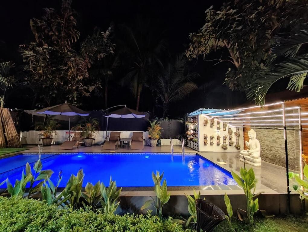 A swimming pool with a stone wall and a Buddha statue, surrounded by greenery and outdoor seating.