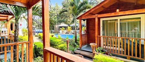 Una terraza de madera con piscina y abundante vegetación.
