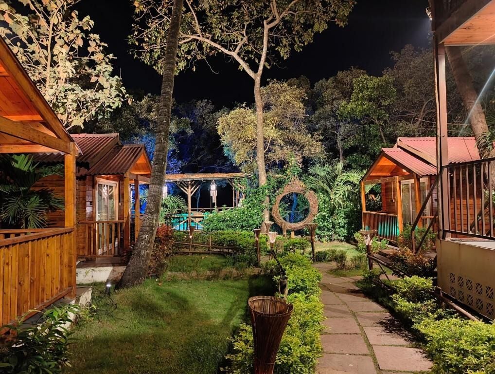A nighttime view of a resort with wooden cabins, a central circular structure, and a well-maintained garden.
