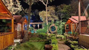 A nighttime view of a resort with wooden cabins, a central circular structure, and a well-maintained garden.