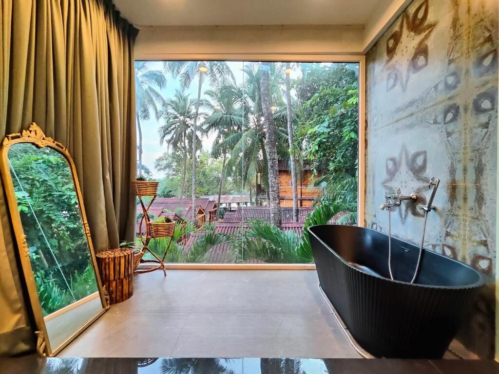 Una habitación con un ventanal grande, una bañera negra, un espejo y vistas a palmeras y edificios.
