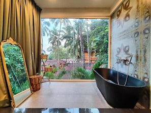 Una habitación con un ventanal grande, una bañera negra, un espejo y vistas a palmeras y edificios.