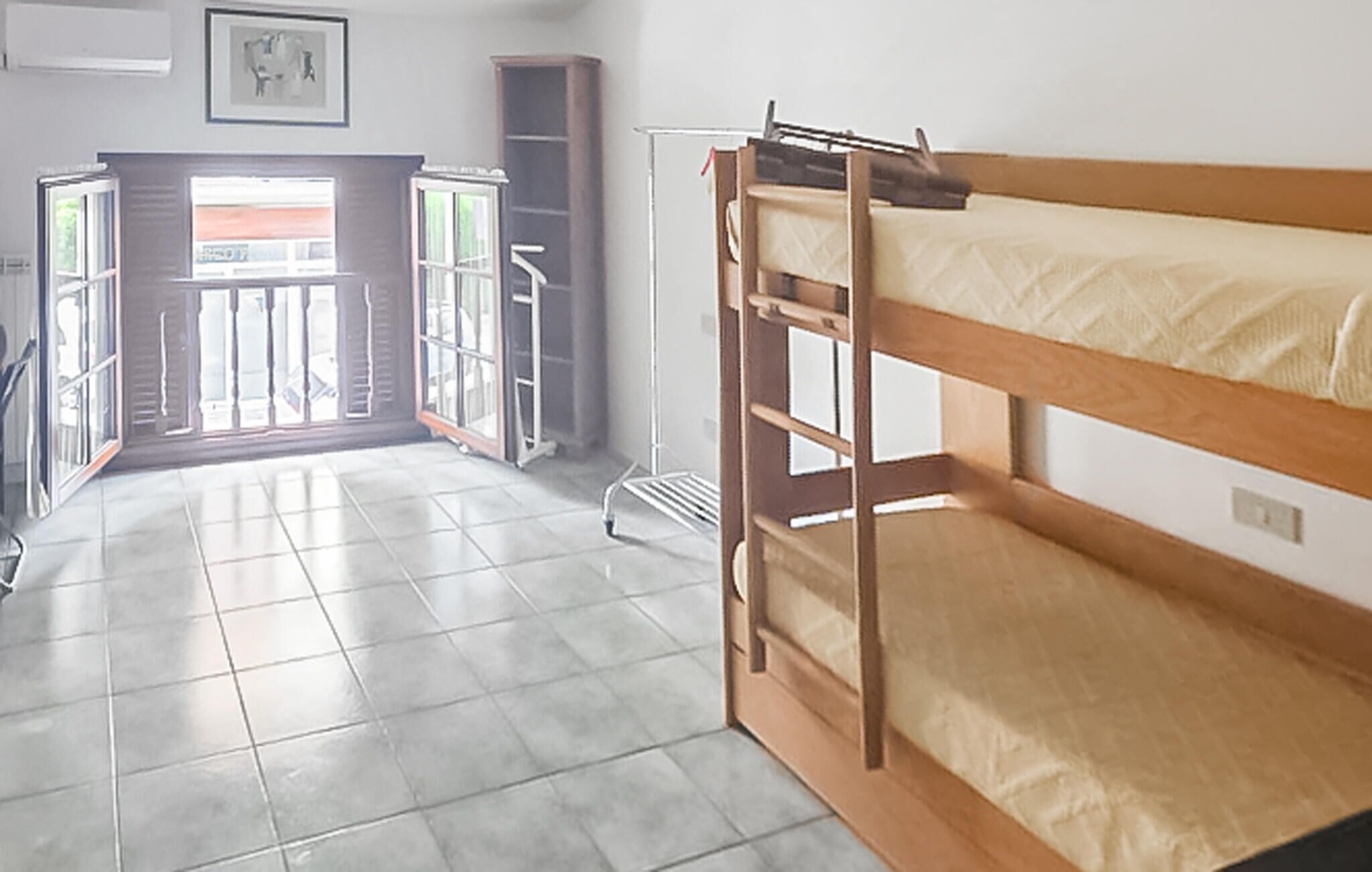 A room with a bunk bed, a door leading to a balcony, and a window with blinds.