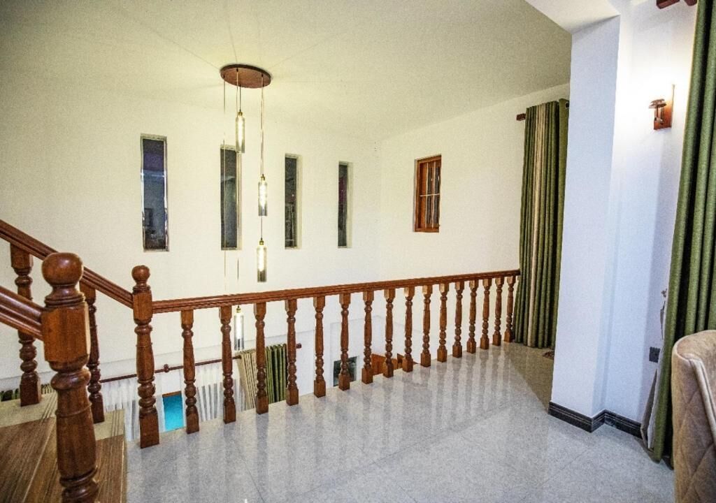 Un interior espacioso con una escalera de madera, un radiador y vista a una cortina verde.