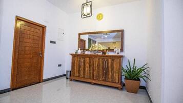 Un couloir avec une porte en bois, une armoire contenant des objets décoratifs, un miroir et une plante en pot.