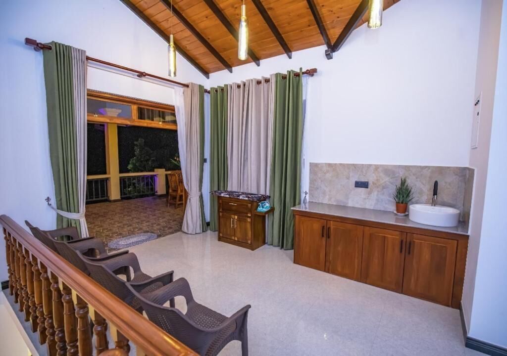 Ein Zimmer mit einer Holztreppe, einer Küchenzeile mit Spüle und Schränken sowie einer Sitzecke mit Stühlen.