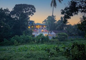 A multi-story building with a balcony, surrounded by lush greenery and trees.