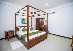 A four-poster bed with a wooden frame, a desk with a chair, and a cabinet in a hotel room.
