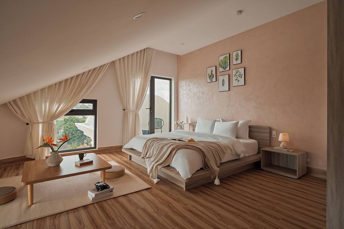 Un dormitorio con cama, mesita de noche, lámpara y ventana con cortinas.