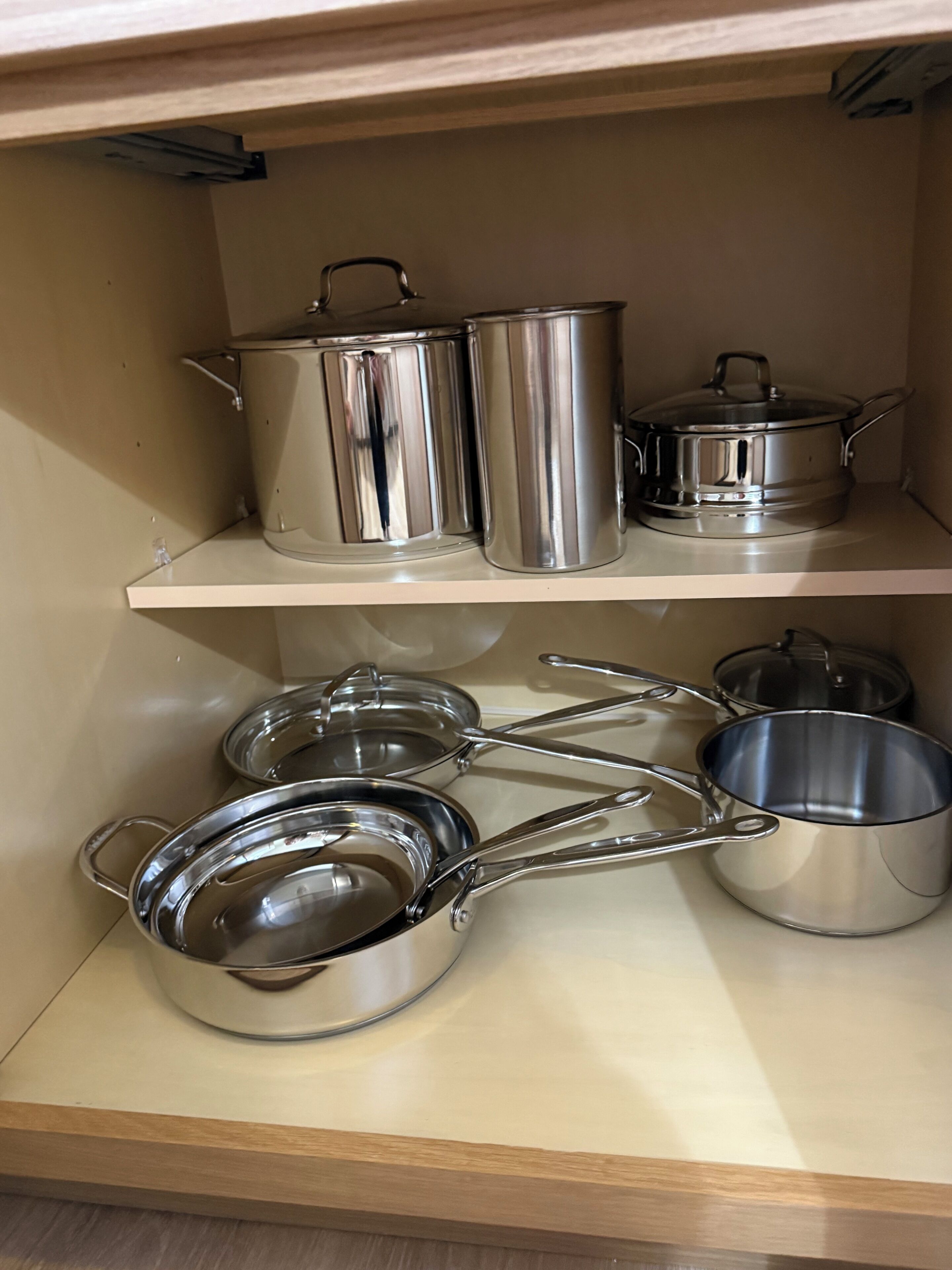Un armario de cocina con utensilios de acero inoxidable, incluyendo ollas, sartenes y tapas.